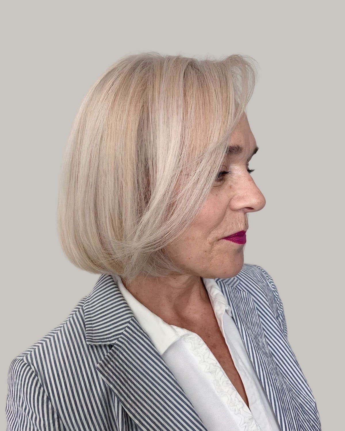 Woman with a pale blonde bob in a striped blazer, in three-quarter view