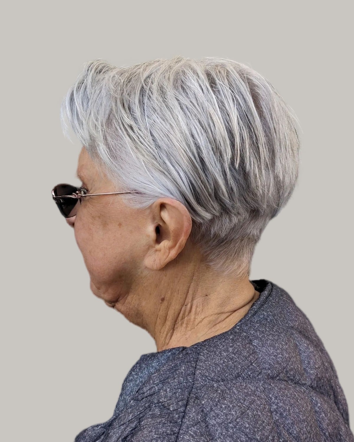 Woman with a silver layered pixie and dark glasses, seen from the side