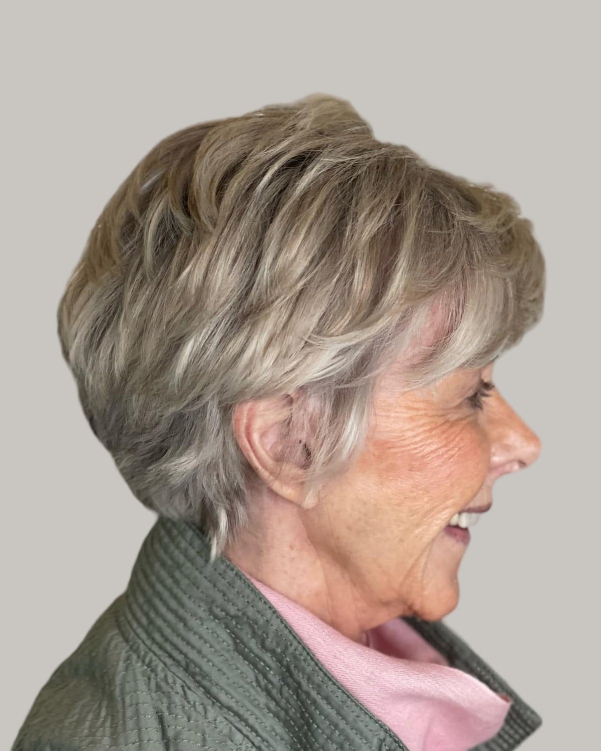 Smiling woman with an ash-blonde layered pixie, in profile