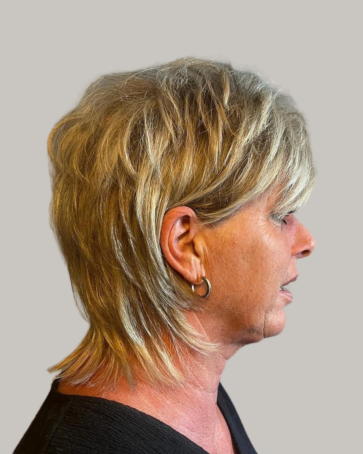Woman with a golden-blonde mixie and hoop earrings, seen in profile