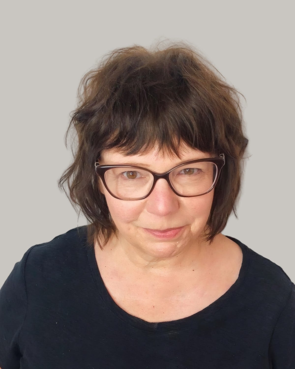 Woman with a dark brown shag, full bangs and black glasses