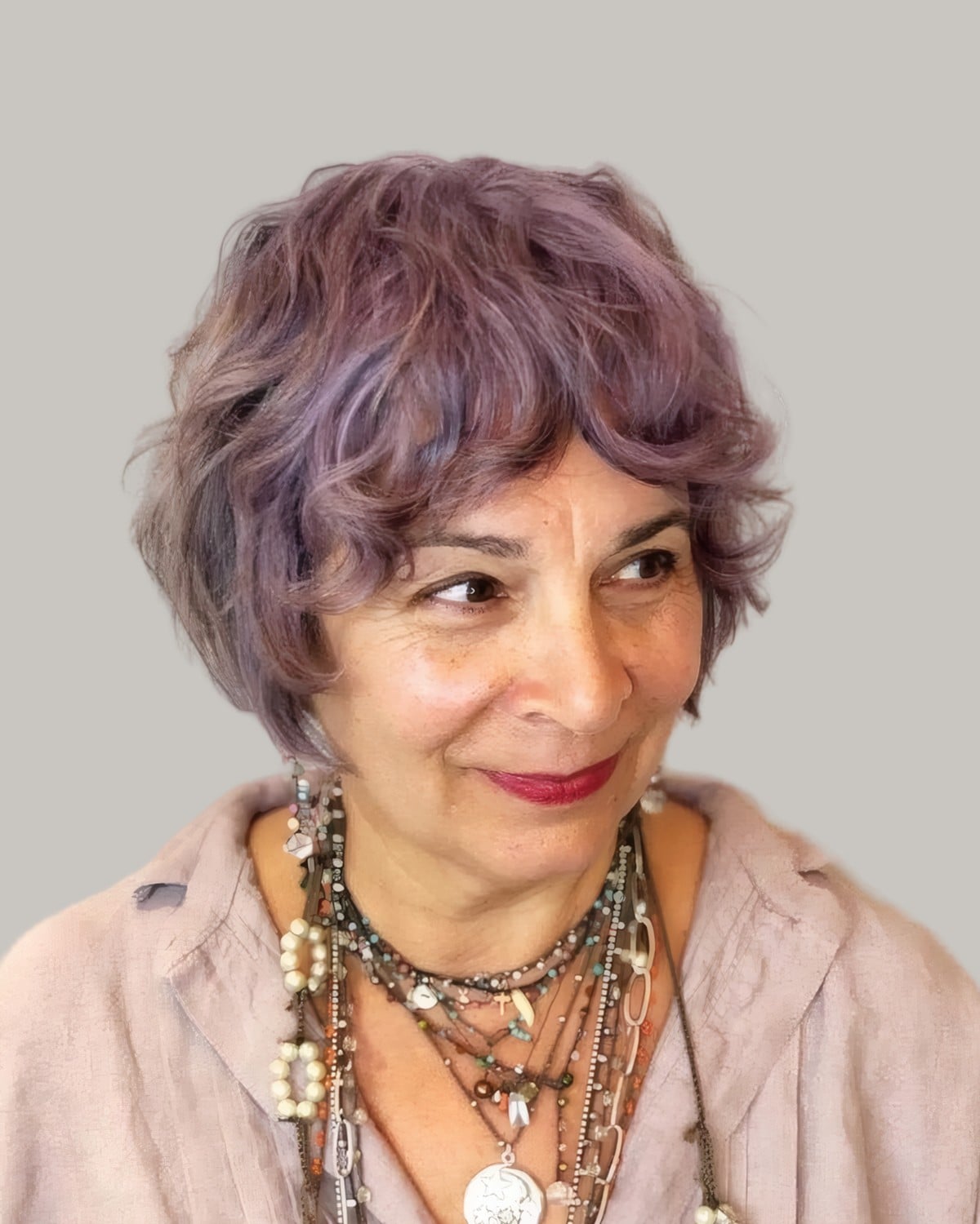 Smiling woman with a lilac curly bob and layered necklaces