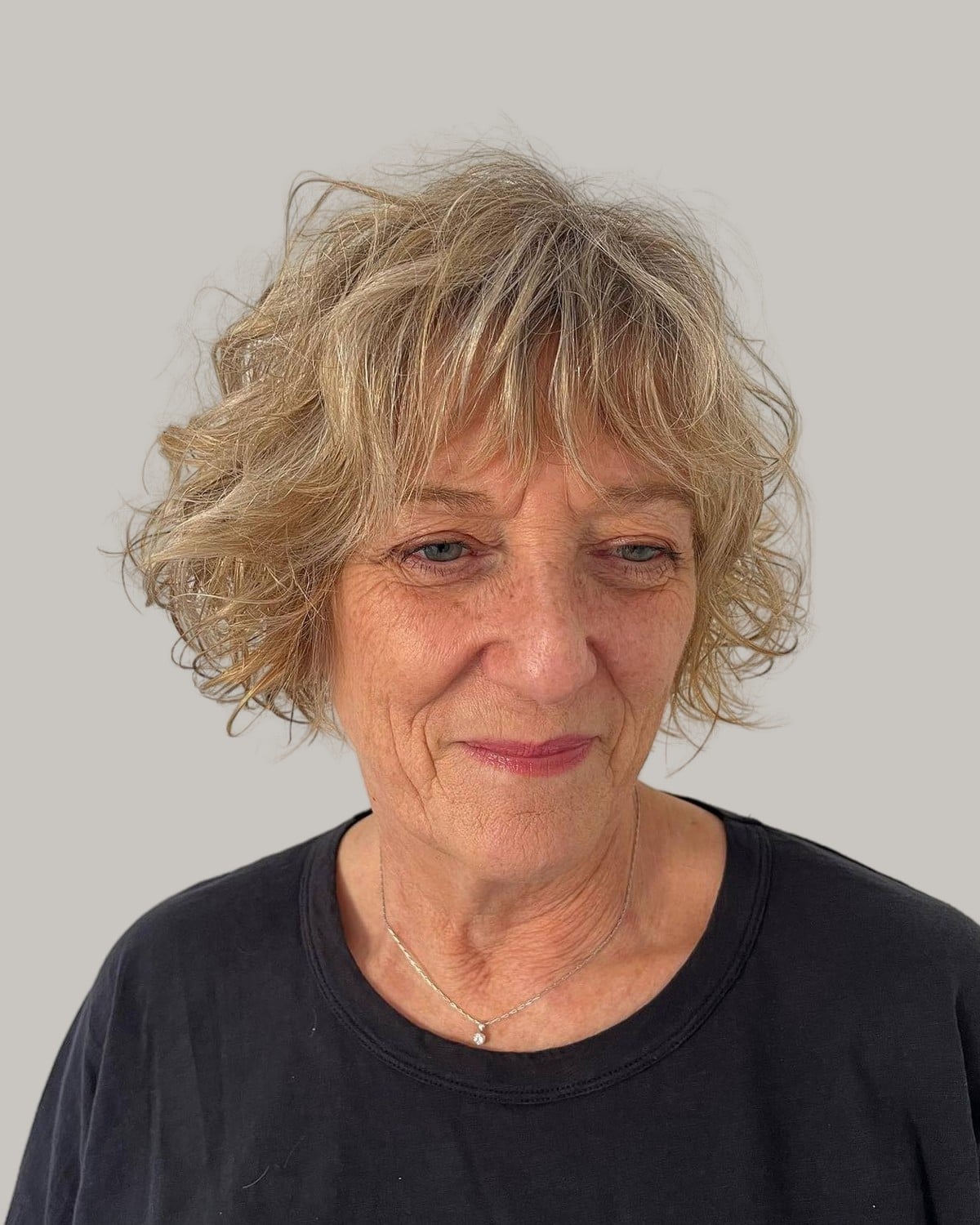 Woman with short blonde curls and a curly fringe, in a black top