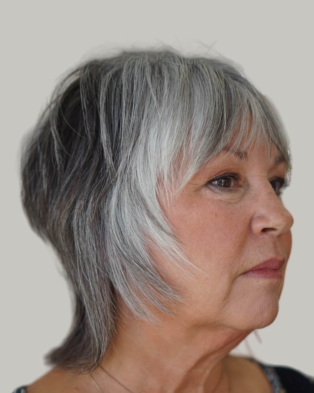 Woman with a gray and silver shag and long bangs, in three-quarter view