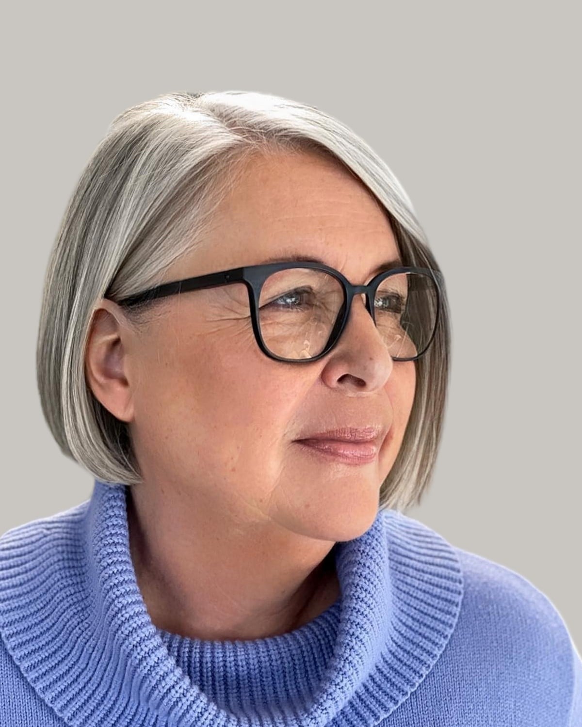 Woman with a silver bob, black glasses and a periwinkle turtleneck