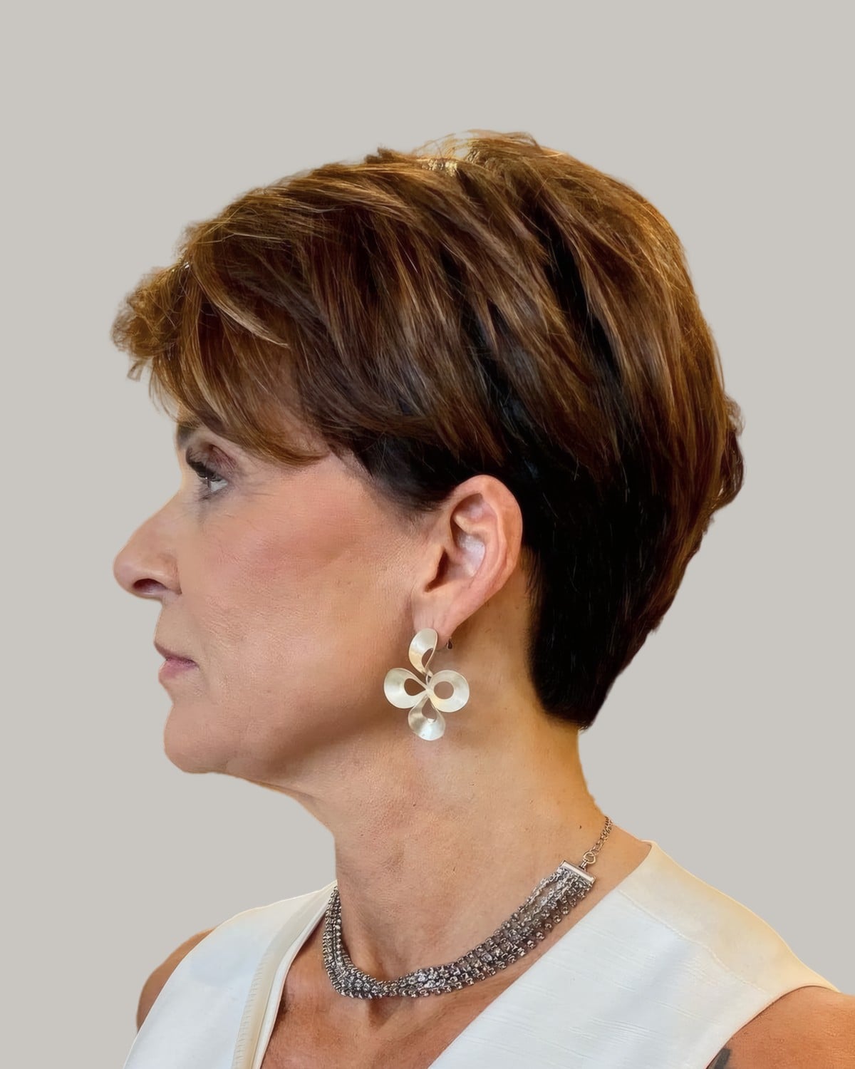 Woman with a chestnut pixie and a statement earring, seen in profile