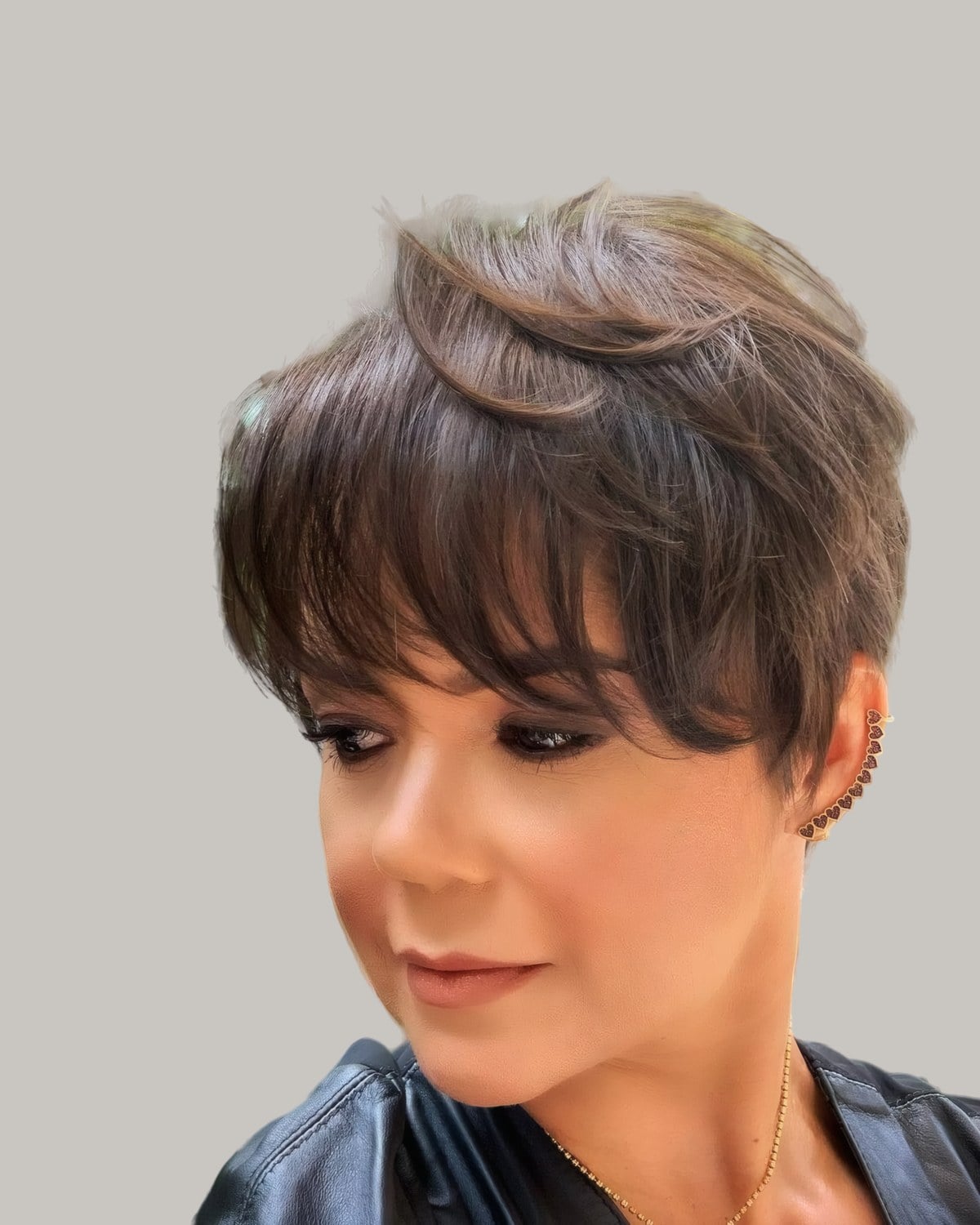 Woman with a brown feathered pixie and a long swept fringe, looking down