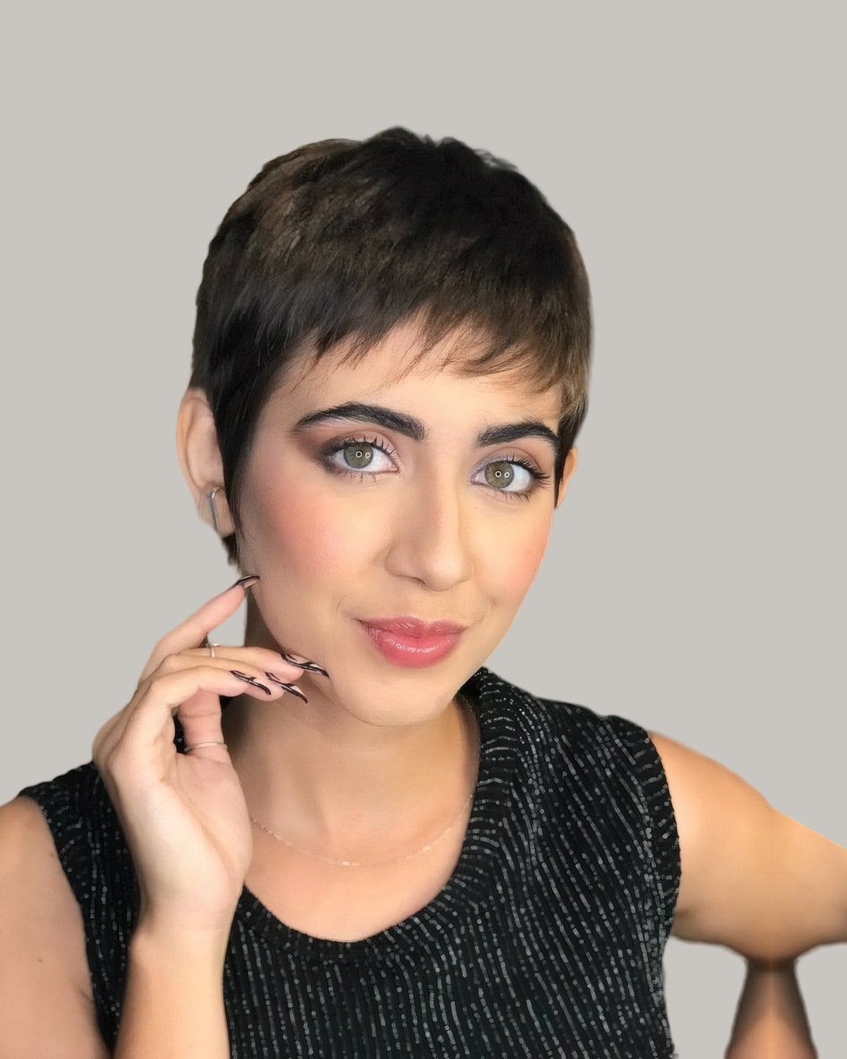 Woman with a short dark pixie and baby bangs, hand at her cheek