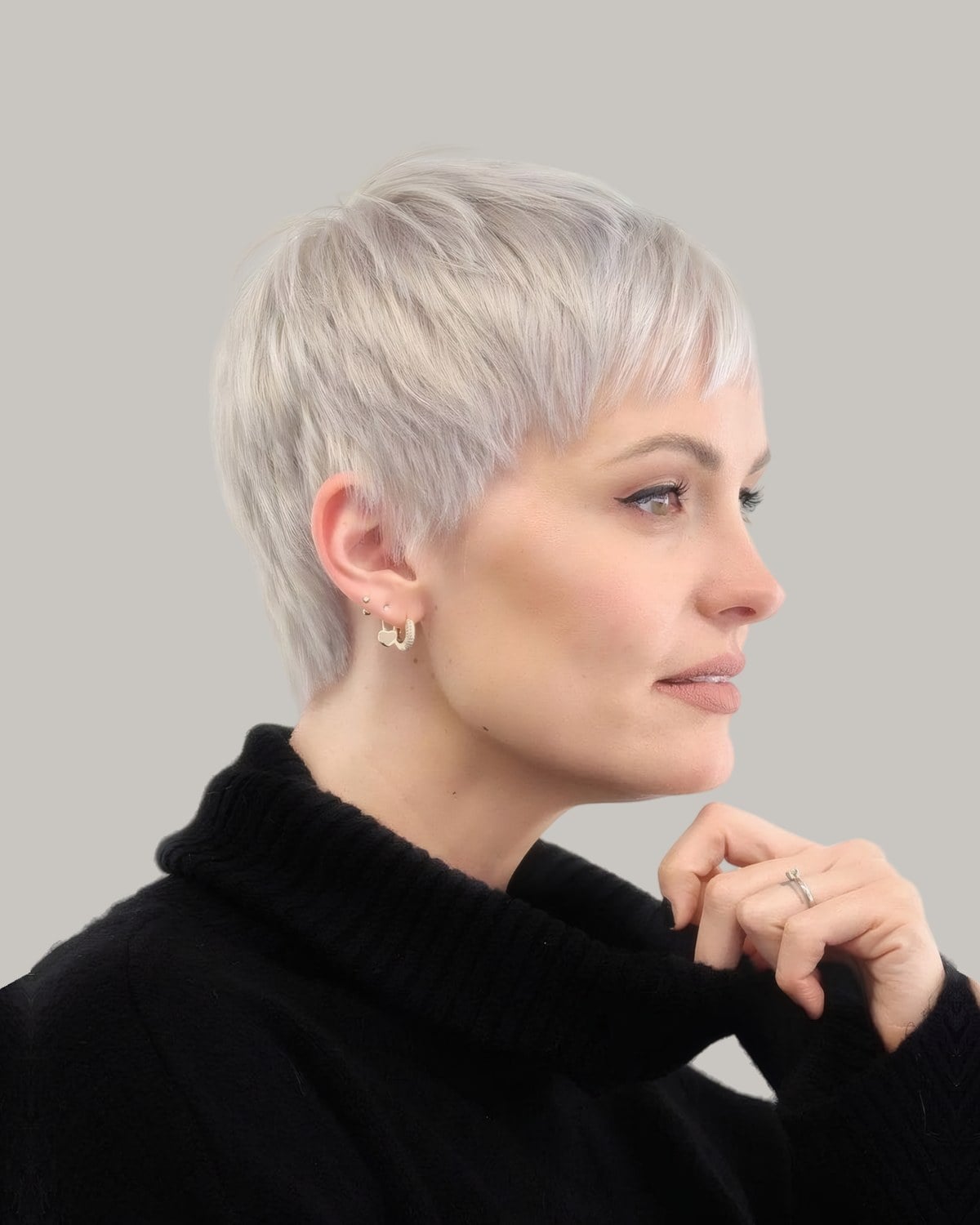 Woman with a platinum pixie and a wispy fringe, hand at her chin