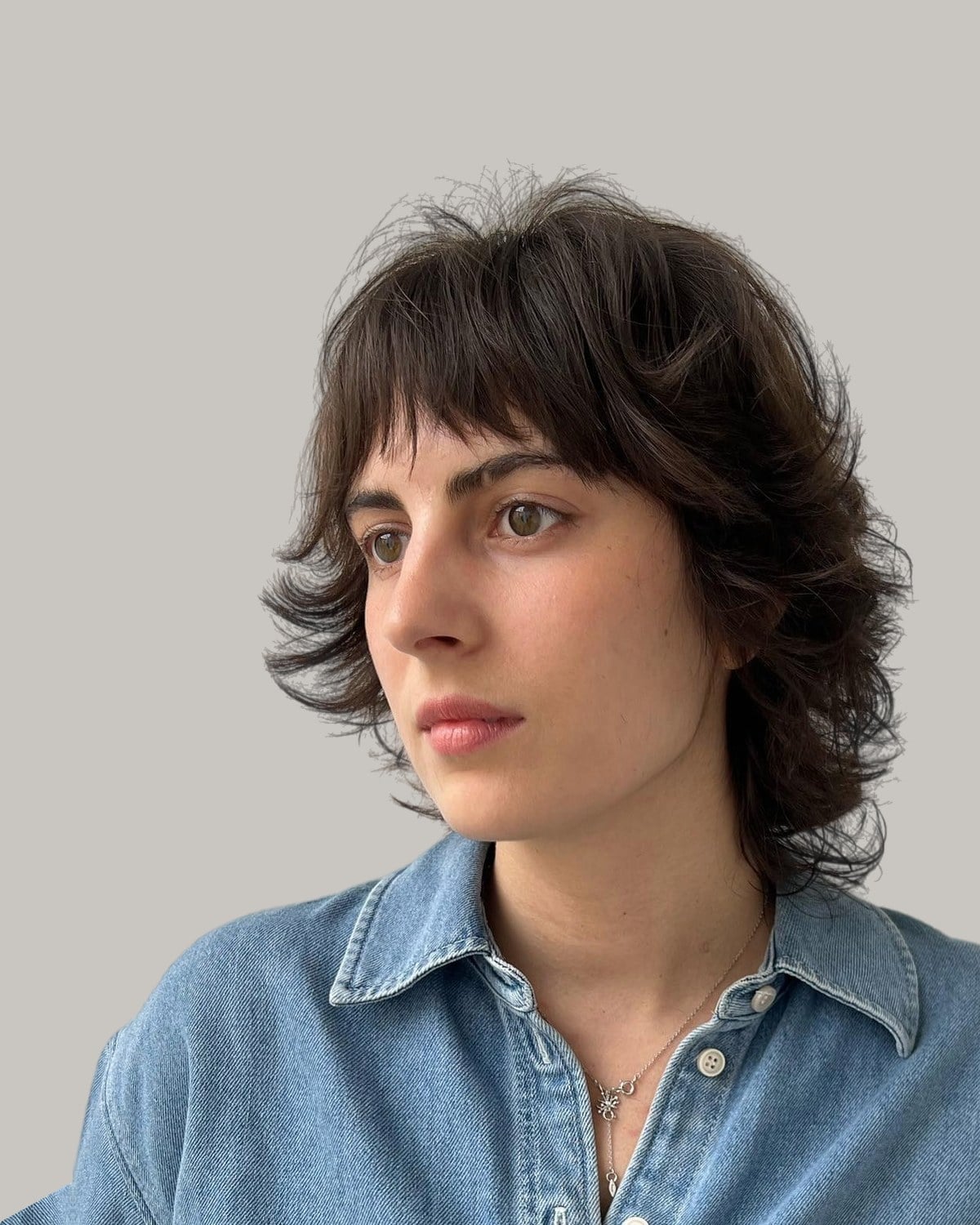 Woman with a dark short wolf cut and piecey bangs, looking to the side