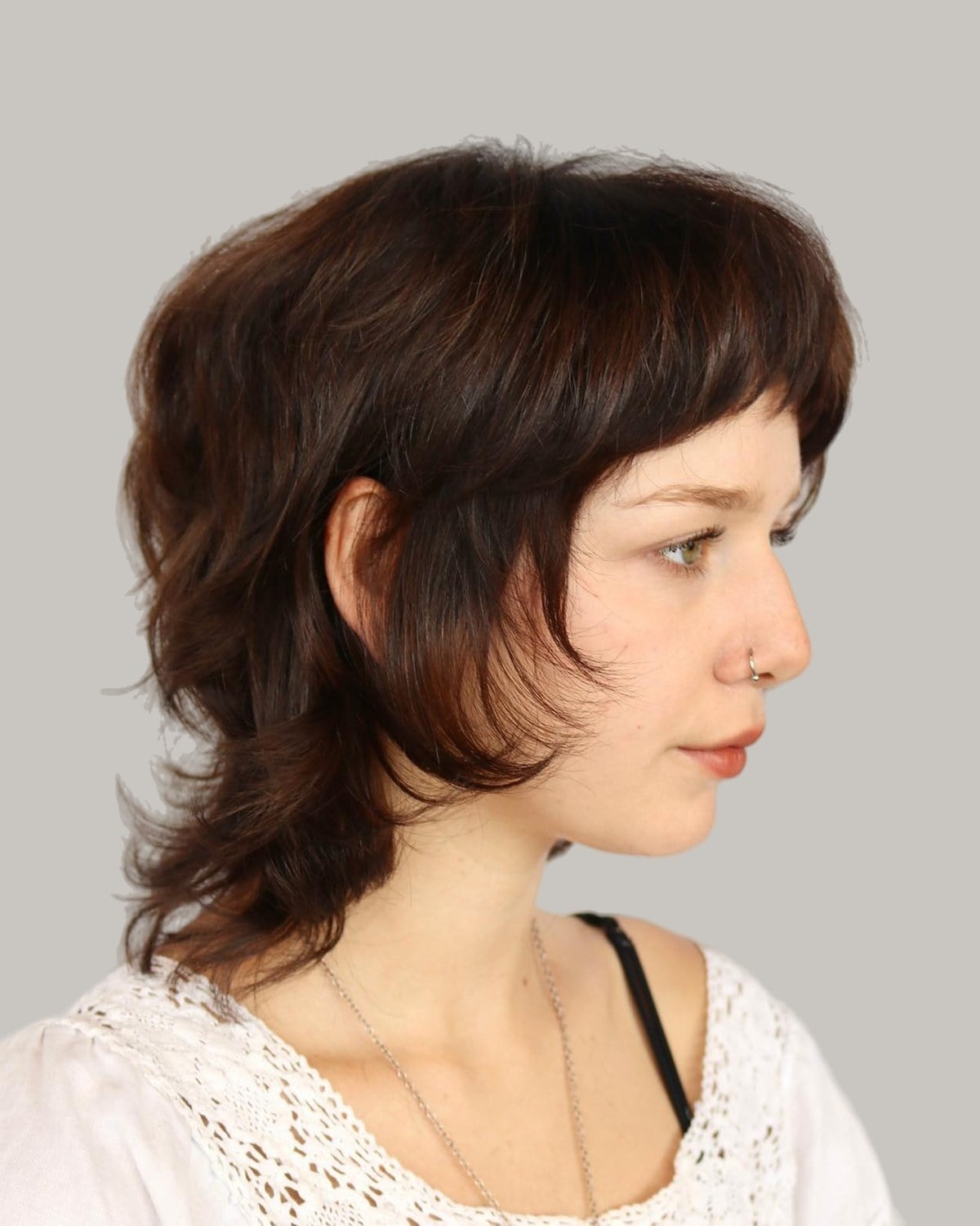 Woman with a brown short wolf cut and curtain bangs, in profile