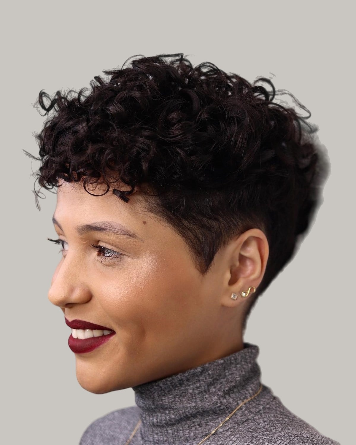 Smiling woman with a tapered curly cut and a clipped side, in profile