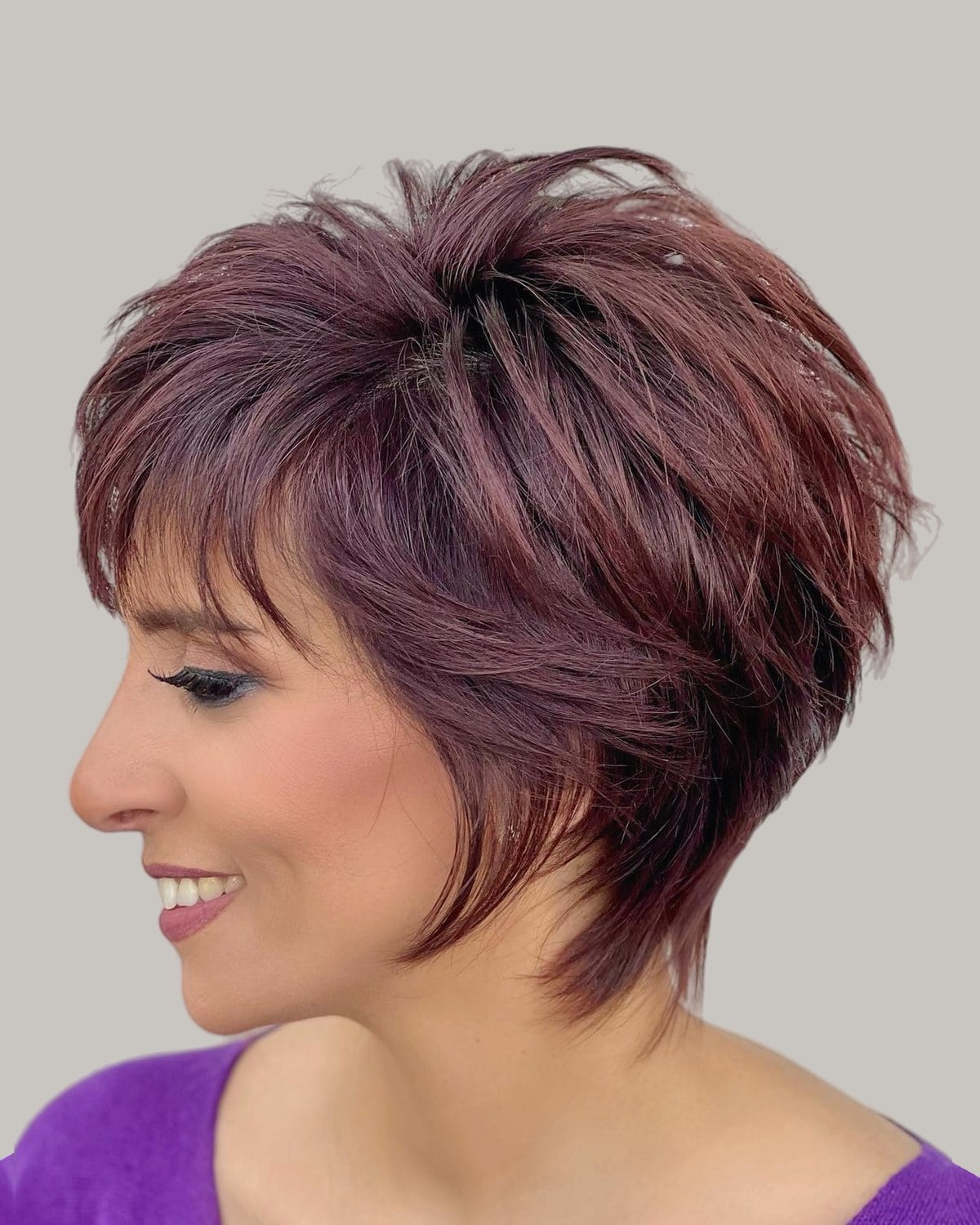 Smiling woman with a burgundy layered pixie and a side fringe