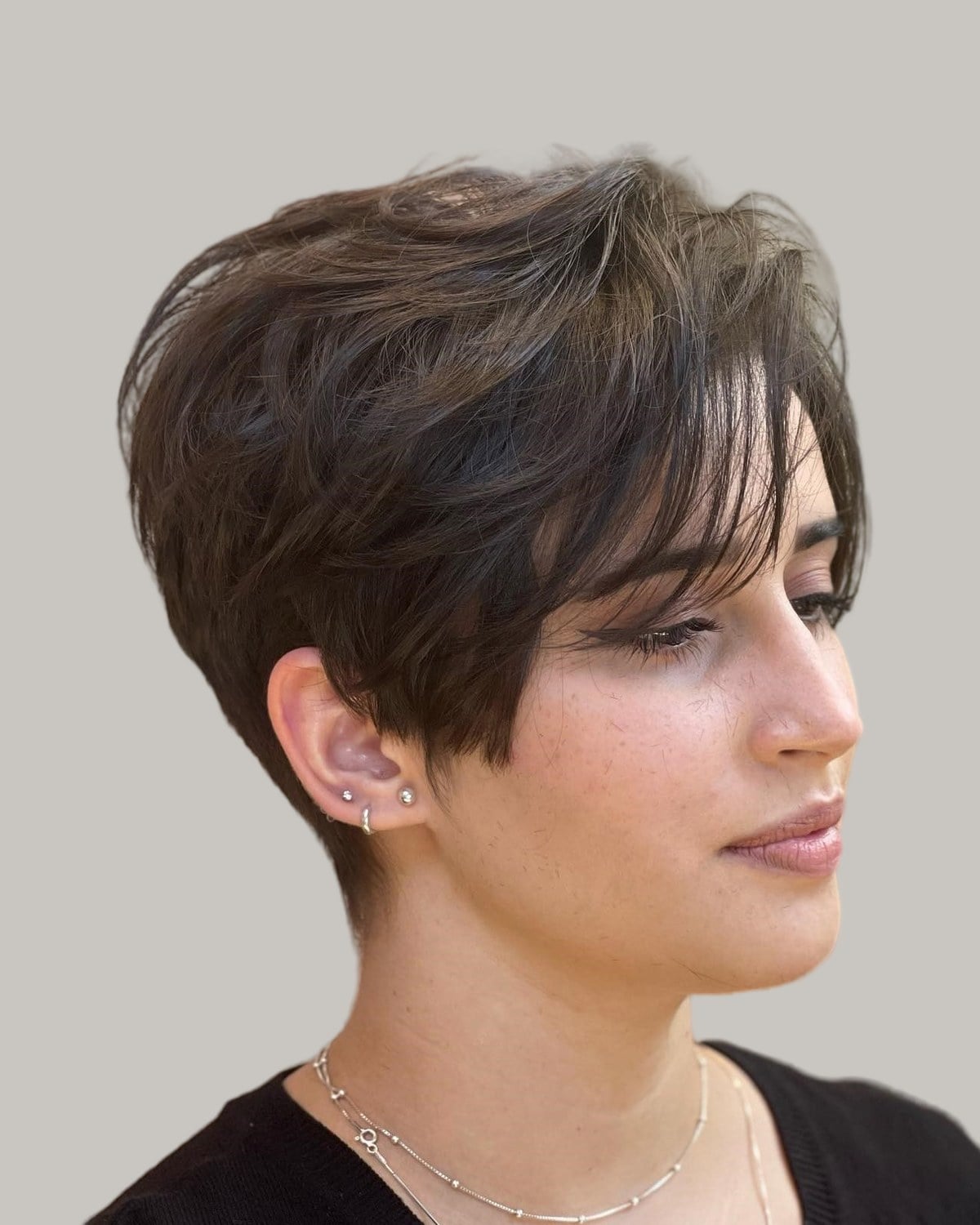 Woman with a brown layered pixie, looking to the side