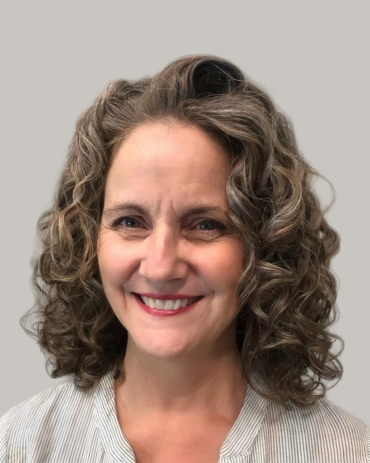 Smiling woman with brown curly hair to the shoulders, gray threaded through
