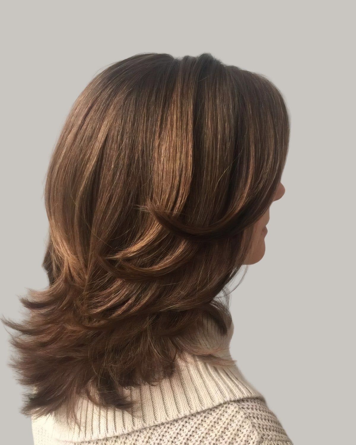 Woman with brown hair and caramel highlights, each layer flipped out, seen from behind