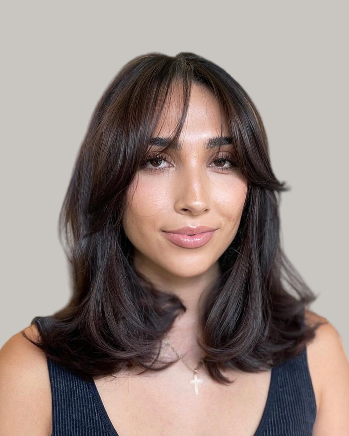Woman with dark brown hair just past the shoulders, curtain bangs and flicked layers