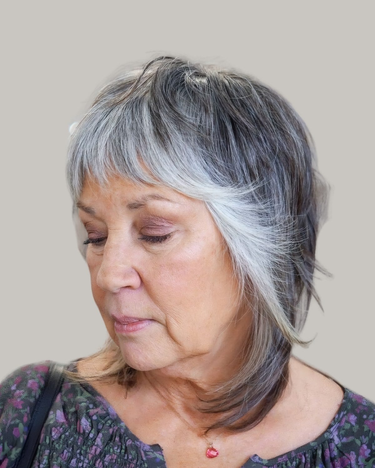 Woman with a salt-and-pepper feathered shag and wispy bangs, looking down