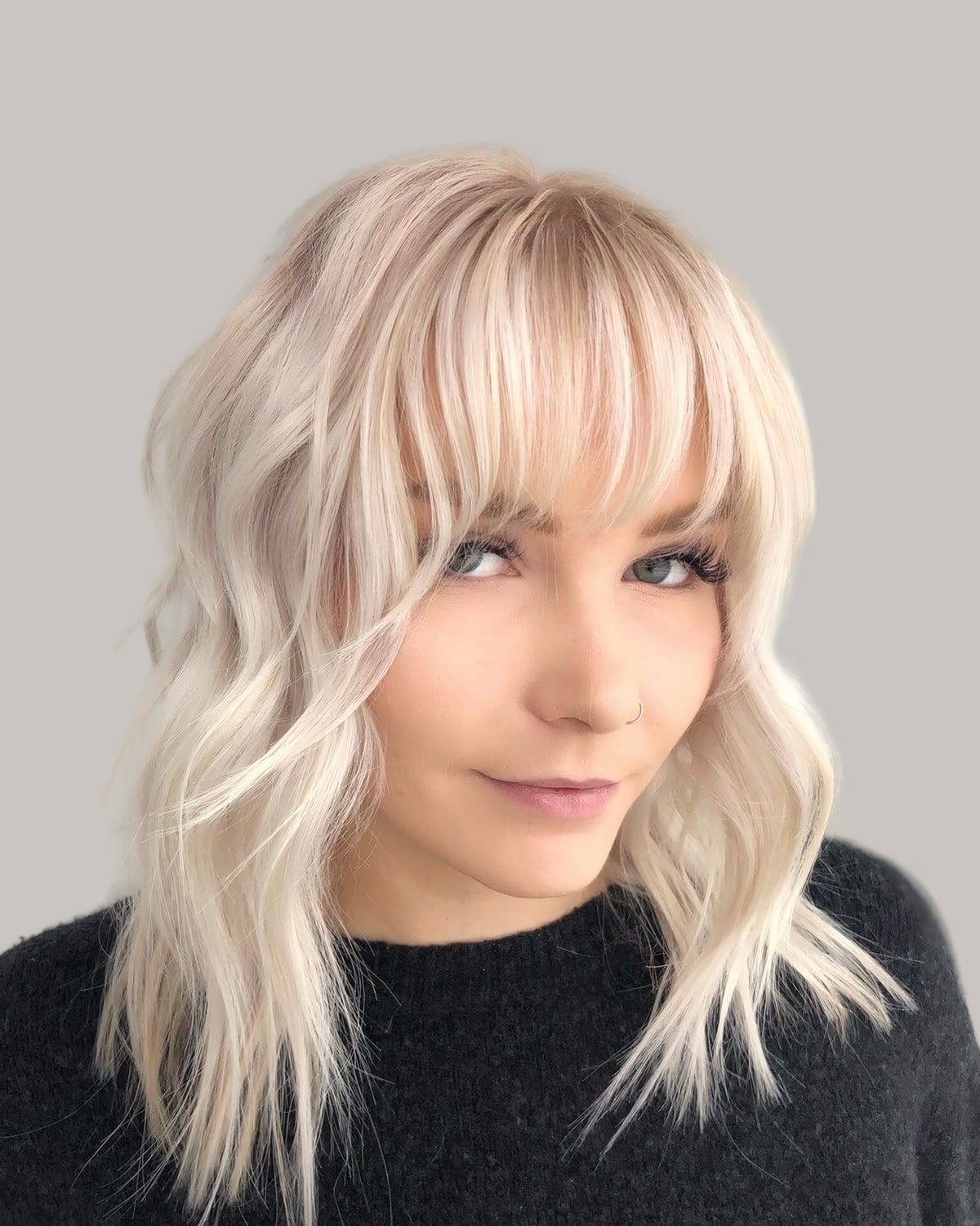 Woman with golden and platinum blonde hair in loose waves and wispy bangs