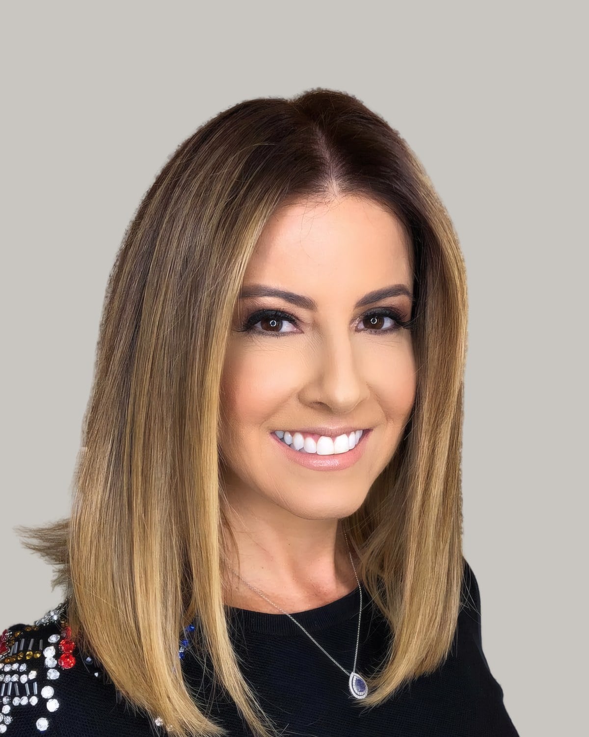 Smiling woman with straight shoulder-length hair, a darker root and blonde highlights