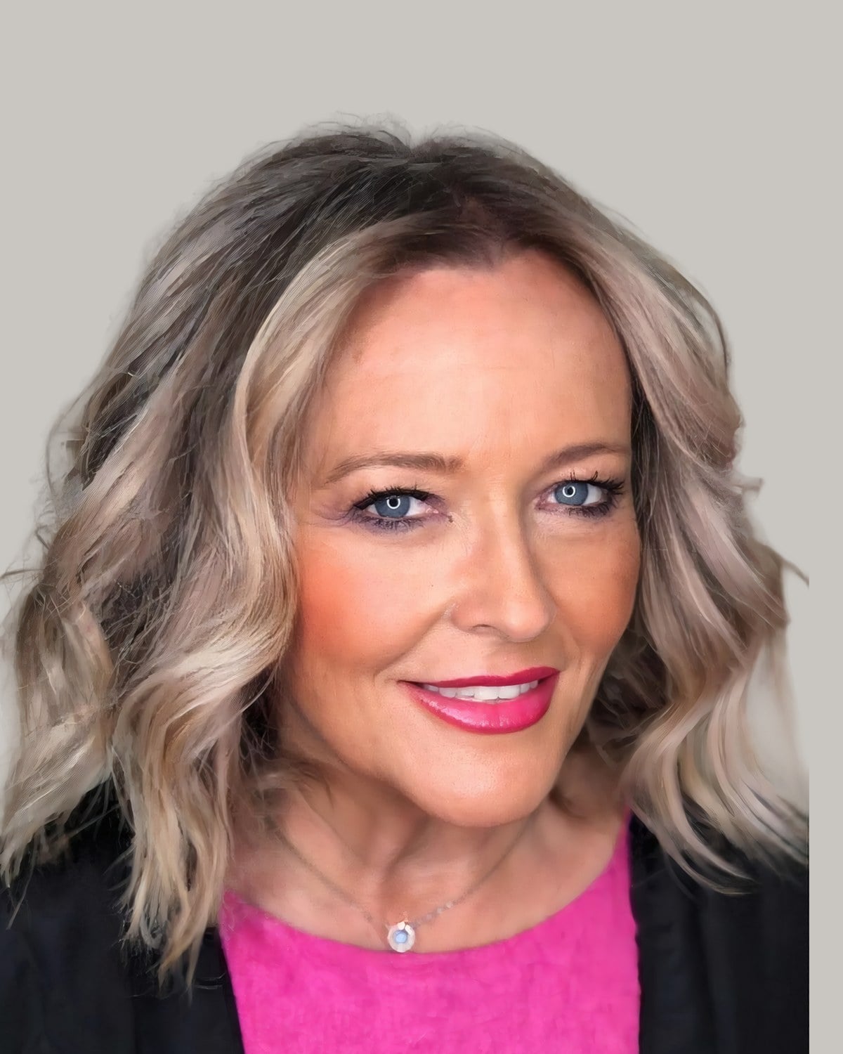 Smiling woman with bronde shoulder-length waves and a pink sweater